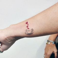 a woman's arm with a coffee cup and hearts tattoo on the left forearm