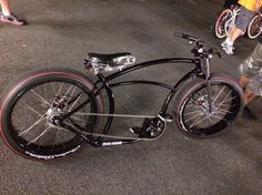 a black bike with red rims parked on the street next to people walking by