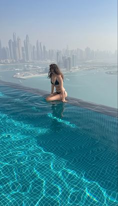 a woman sitting on the edge of a swimming pool in front of a city skyline