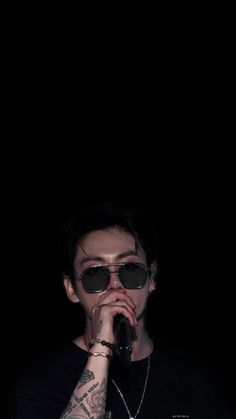 a man with tattoos on his arm holding a microphone in front of his face and wearing sunglasses