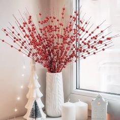 a white vase filled with red berries on top of a table next to a christmas tree