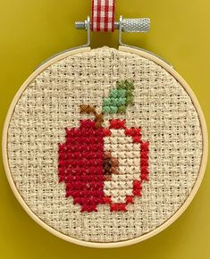 a cross stitch apple with a red and white striped ribbon hanging from it's hoop