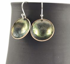 "A beautiful delicate pair of bronze green \"bowl\" shaped earrings hanging on sterling silver 925 hook wires, perfect for everyday wear. Copper discs were domed into little \"bowls\" and filled with bronze enamel and fired at 900 degrees. Several layers of enamel were applied to create patterns, depth and colour. The back of the earrings have been enamelled in black to provide strength and comfort. A perfect way to add a pop of colour to your jewellery collection or a gift for someone special. Green Round Pendant Earrings For Gift, Round Enamel Earrings, Nickel-free Enamel Round Earrings, Sterling Silver Earrings With Black Enamel In Round Shape, Sterling Silver Earrings With Black Enamel, Sterling Silver Round Earrings With Black Enamel, Round Black Enamel Earrings As Gift, Circular Earrings, Bronze Green