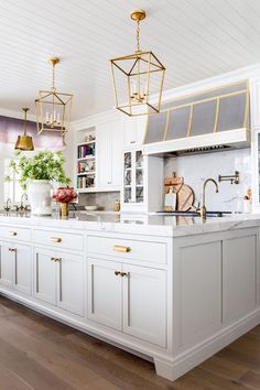 a large kitchen with white cabinets and gold accents on the island countertop, along with brass pendant lights