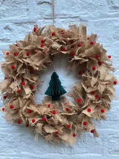 a wreath with a christmas tree hanging from it's center and red berries on the bottom