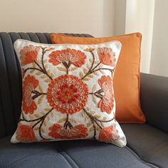 an orange and white pillow sitting on top of a gray couch