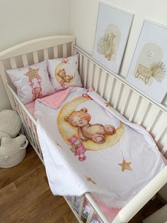 a baby crib with a teddy bear comforter and two pictures on the wall