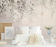 a white bed sitting in a bedroom next to a wall covered in flowers and leaves