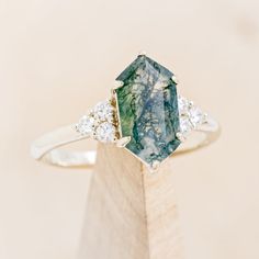 a green and white diamond ring sitting on top of a wooden block