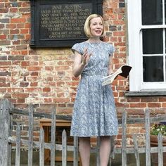 a woman standing in front of a brick building holding a book and talking to someone