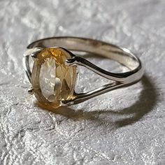 a fancy ring with an oval cut citrine surrounded by thin silver bands on a textured surface