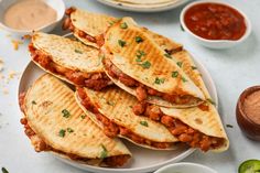 several quesadillas on a white plate with salsa in bowls and condiments