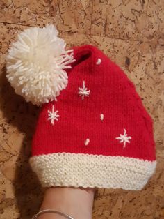 a red and white knitted hat with snowflakes on it, being held by a woman's hand