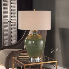 a green vase sitting on top of a glass table next to a lamp and chair