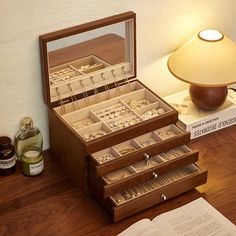 an open jewelry box sitting on top of a wooden table next to a lamp and book