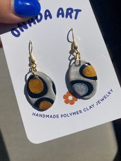 a pair of handmade polymer clay earrings with gold and blue accents on them, sitting in front of a sign