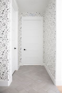 an empty hallway with floral wallpaper on the walls and door to another room behind it