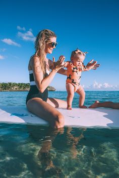 a woman sitting on top of a surfboard holding a baby