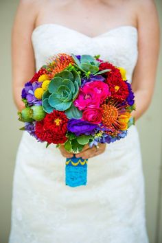 a bride holding a colorful bouquet of flowers and succulents on her wedding day