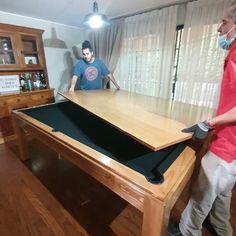 two men are playing pool in the living room while one man is wearing a face mask