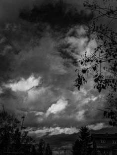 black and white photograph of clouds in the sky above some trees on a cloudy day