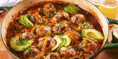 a pot filled with meatballs and vegetables on top of a wooden table next to a glass of beer