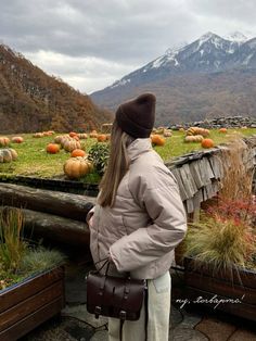 a woman standing on top of a roof next to lots of plants and pumpkins