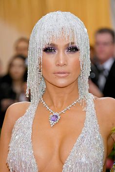 a woman with white hair and purple eyeshadow, wearing a silver necklace that has fringed beads on it