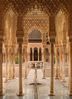 the inside of an ornate building with columns and arches on either side, there is a fountain in the middle