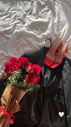 a bouquet of red roses sitting on top of a bed next to a black jacket