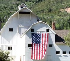 an american flag hanging on the side of a white barn with mountains in the background