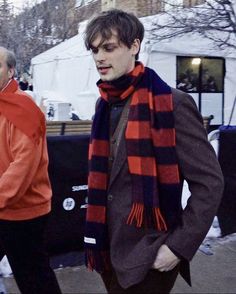 a man in an orange jacket and scarf walking down the street with his hand on his hip