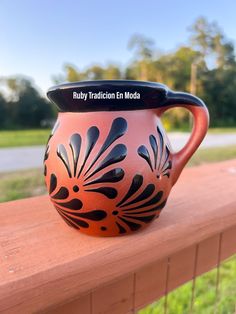 a red and black vase sitting on top of a wooden fence