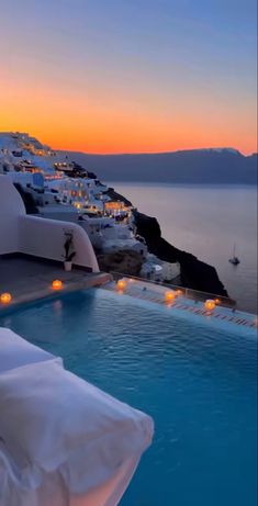 an outdoor swimming pool with candles lit in the water next to white buildings at sunset