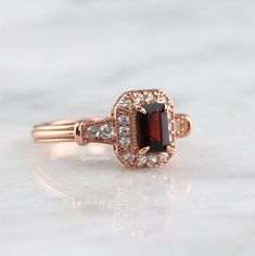 Gorgeous Vintage Inspired Garnet Ring ►Made of solid sterling silver with the 14k rose gold finish (925) ►Accented With Simulated Diamonds (CZ) ►Average band width: 2.3 mm ►Halo size: 9.9mm x 8.3mm Center Stone: Garnet Stone Cut: Emerald Measurements: 4.0 x 6.0 mm Carat Weight: 0.7 ct. (approx.) Gemstone creation: 100% Natural Hardness: 7.5 (Mohs scale) ►Average band width: 1.6 mm ►Please be aware that plated jewelry can wear off over time, if this is a concern we would suggest going with the st Antique Promise Rings, Garnet Engagement Ring, Natural Opal Ring, Mohs Scale, Red Gemstones, January Birthstone, Garnet Ring, Birthstone Gifts, Garnet Stone