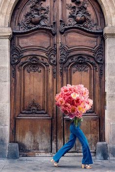 a woman walking past a large wooden door holding a bunch of flowers in her hands