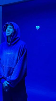 a man standing in front of a blue wall wearing a hoodie and black sweatpants