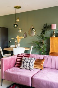 a living room filled with furniture next to a dining room table and two lamps hanging from the ceiling