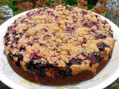 a cake with crumbs and blueberries on a white plate in front of some flowers