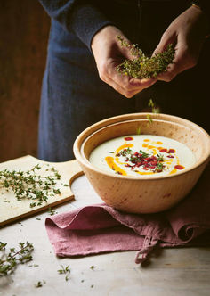 a person is sprinkling herbs on top of a bowl of soup in front of a cutting board