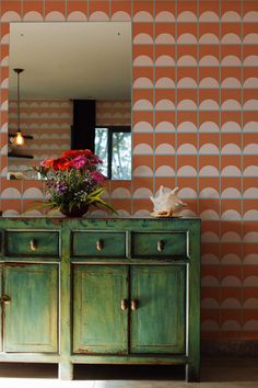 a green dresser with flowers on top in front of an orange wallpapered room