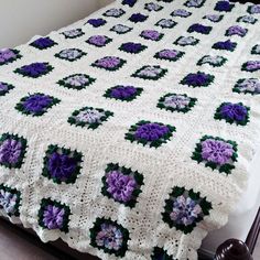 a crocheted blanket with purple and green flowers on the bottom is laying on a bed