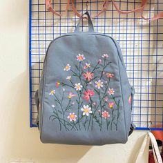 a blue backpack with flowers painted on it hanging from the wall next to a pair of glasses