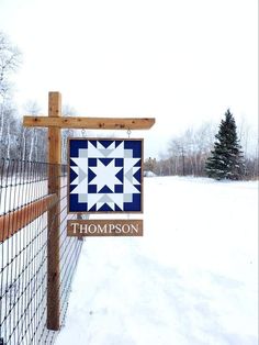 a wooden fence with a quilt hanging on it's side in front of a snow covered field