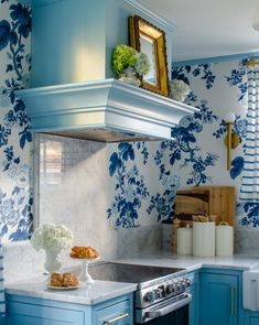 a blue and white kitchen with floral wallpaper on the backsplash, stove top oven and sink