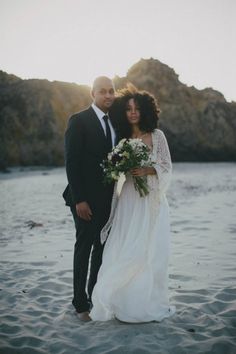 a man and woman standing on top of a beach next to each other holding flowers