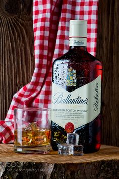 a bottle of ballantines sitting on top of a wooden table next to two glasses