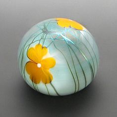 a glass ball with yellow flowers painted on the outside and inside, sitting on a gray surface