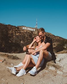 a man and woman sitting on the ground in front of hollywood blvd sign