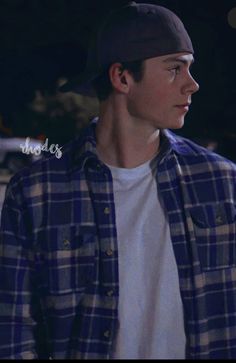 a young man wearing a plaid shirt and black hat standing in the street at night